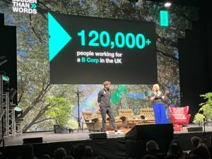 Presenters in front of a screen saying 120,000 plus people working for a b corp in the UK